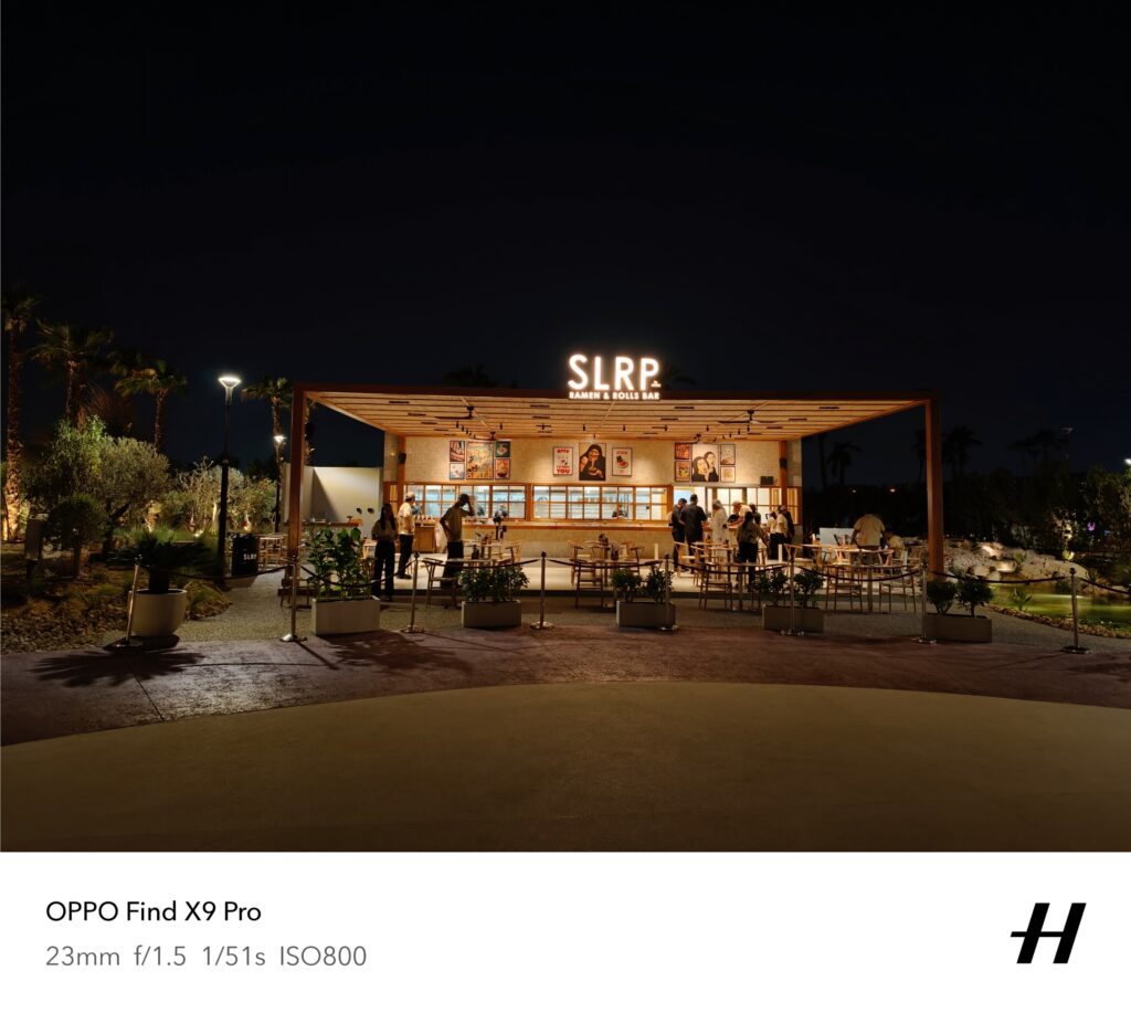 A wide angle shot of a restaurent at night - names SLRP (visible on the signboard) all illuminated with warm lights.