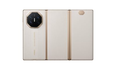 A back view of the Huawei Mate XT Ultimate Design smartphone in a fully unfolded state. The device features three distinct panels with a cream-colored, textured leather finish. The left panel houses a large, octagonal gold-rimmed camera module with "XMAGE" branding and four lenses. The words "HUAWEI" and "ULTIMATE DESIGN" are embossed vertically in gold on the leather. The hinges are visible as slim gold vertical lines connecting the panels.