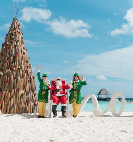 A professional lifestyle photograph at Nova Maldives during the 'Maldivian Magic' festive season, featuring a unique sustainable Christmas tree handcrafted from tiered cajon wood and driftwood.