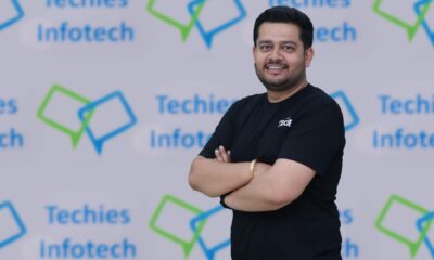 Anurag Byala, CEO, Techies Infotech, guy in black tee shirt standing infront of Techies Infotech logo
