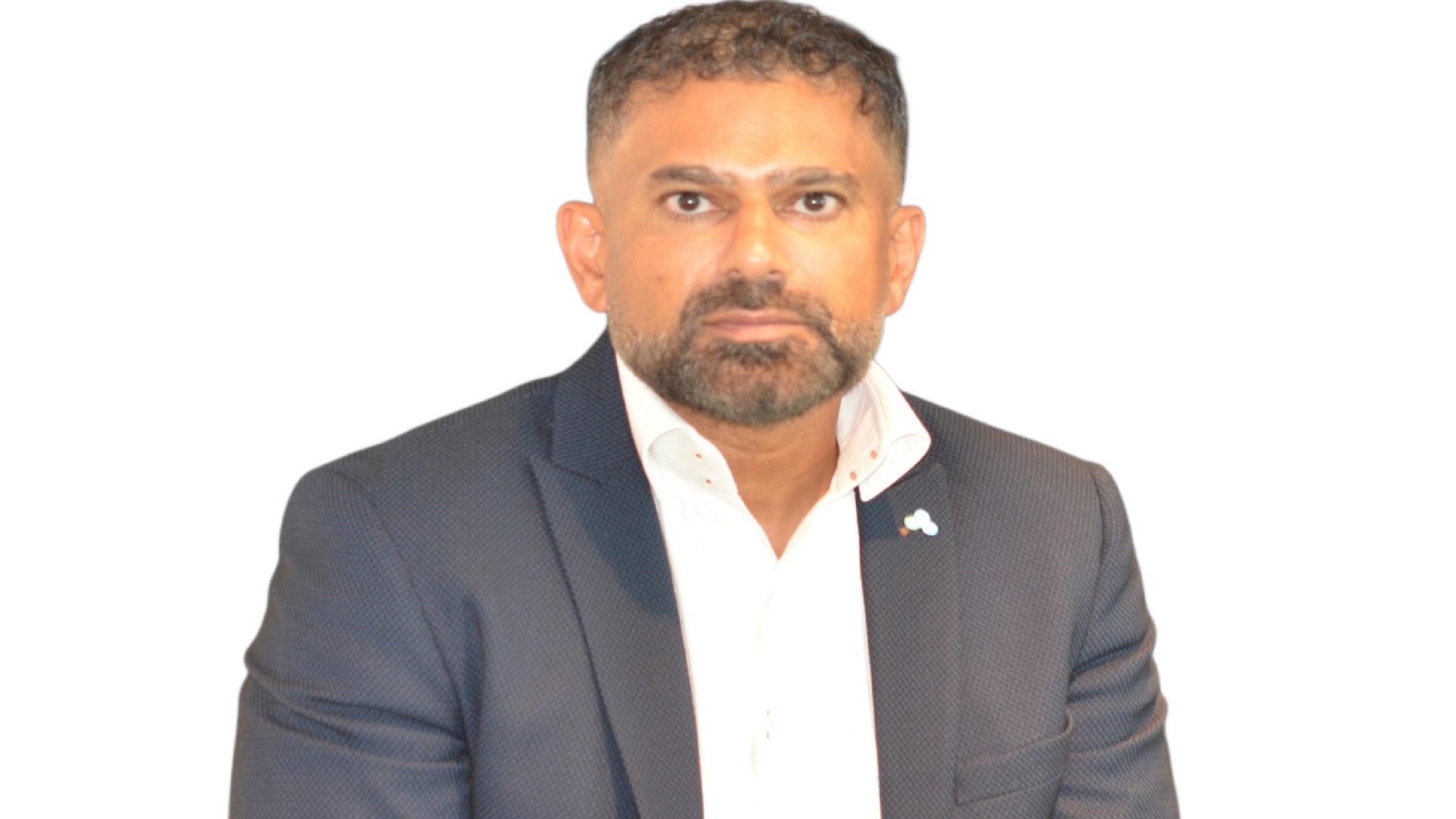 A person wearing a dark navy textured blazer over a white dress shirt, seated against a plain white background. The blazer features a small lapel pin with a blue and white design