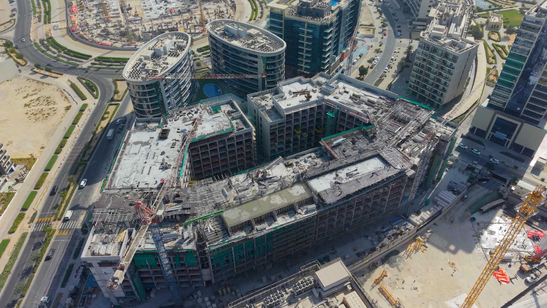 Aerial construction progress shot of the TOWNX Ashley Hills project in Arjan, Dubai, showing the multi-story concrete structure approximately 40% complete with visible construction cranes and scaffolding.