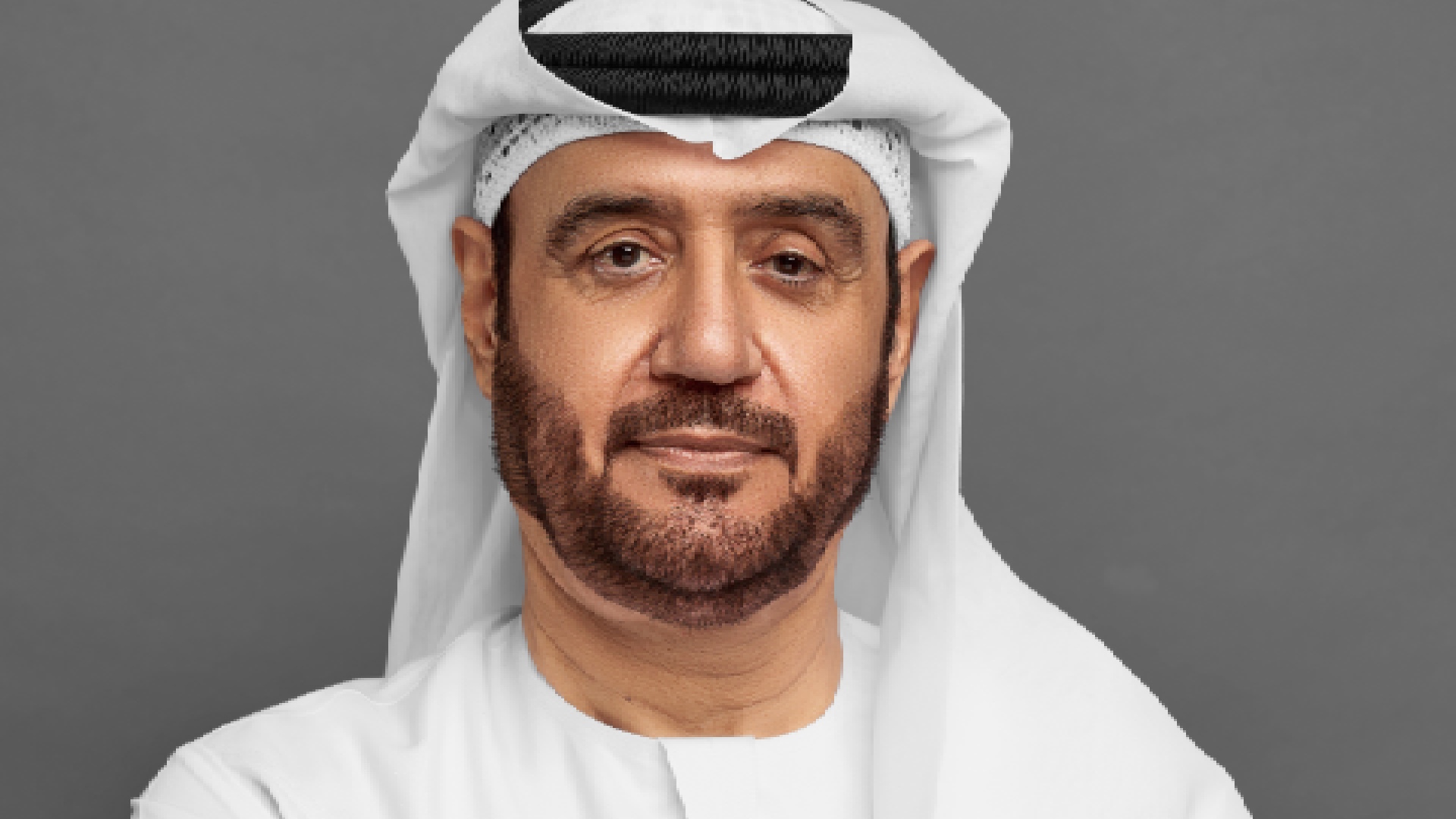 Person wearing a traditional white kandura and ghutra standing on an ornate staircase with decorative black and gold railing inside a bright, elegant interior featuring white walls and intricate architectural details. it is Abdulrahman Abdulla Alhelo Alsuwaidi Co-founder & Chairman, Nabni Developments