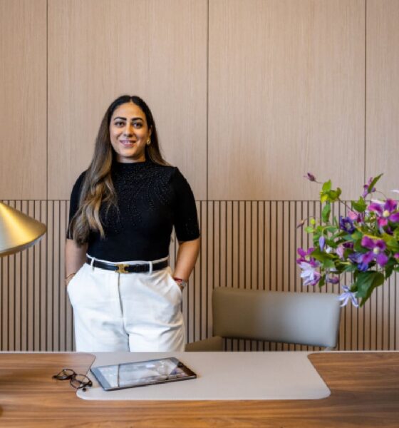 A professional portrait of an architectural or interior designer, likely the founder of KAD Designs, dressed in a business suit and standing in a modern, well-lit interior space.