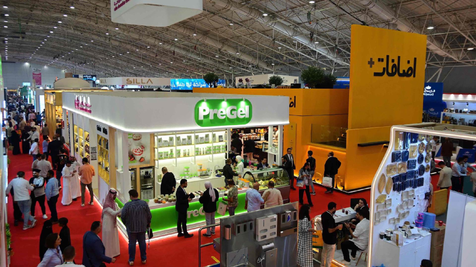 The brightly lit interior of a professional kitchen, featuring chefs gathered around a cooking station during a culinary competition.