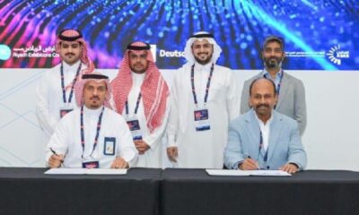 Signing ceremony of a Memorandum of Understanding between Rqeem for Smart Solutions and Torry Harris Business Solutions, with representatives seated at a table signing documents and others standing behind, against a backdrop featuring event branding and digital graphics