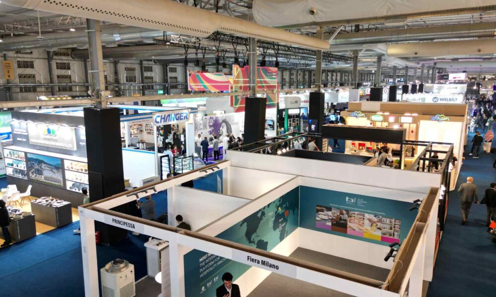 A high-angle, wide-shot of the bustling HORECA Riyadh 2025 exhibition floor at the Riyadh Front Exhibition & Conference Center, showing thousands of professional visitors navigating through 42,000 square meters of sleek corporate booths and hospitality displays under bright industrial lighting