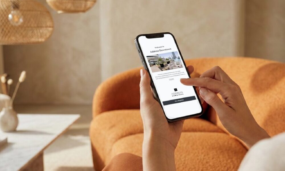 "A close-up, over-the-shoulder view of a person holding a smartphone and using their index finger to interact with the new Address Downtown digital check-in interface