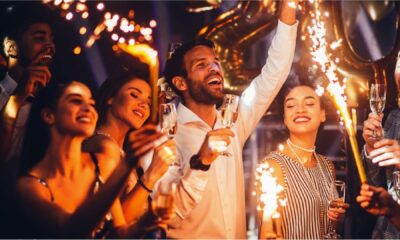 Group of people celebrating and cheering at a party, holding glasses of champagne while sparklers go off in the foreground.