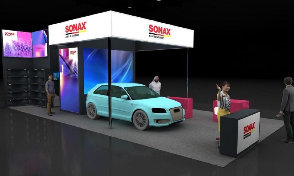 A light blue car displayed under a white canopy at the modern, brightly lit SONAX exhibition booth inside a trade show.
