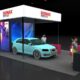 A light blue car displayed under a white canopy at the modern, brightly lit SONAX exhibition booth inside a trade show.