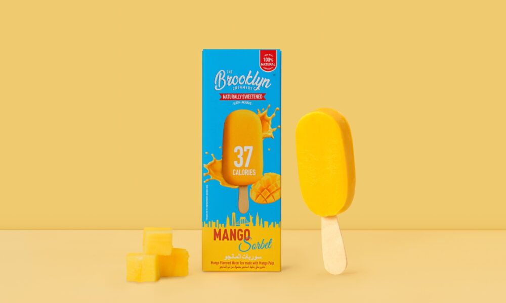 A close-up shot of The Brooklyn Creamery's 37-calorie Mango Sorbet Bar, showing the bright orange sorbet and a partially peeled wrapper on a white background.