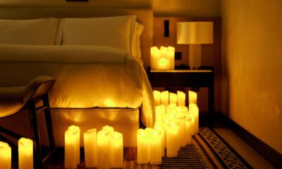A cozy hotel bedroom at Sofitel featuring a white bed with crisp linens, surrounded by numerous glowing pillar candles arranged on the floor and nightstand, creating a warm and intimate ambiance.