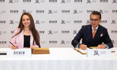 A group of four business professionals, two women and two men, are formally seated at a conference table, posing for a photograph during a signing ceremony or press event.
