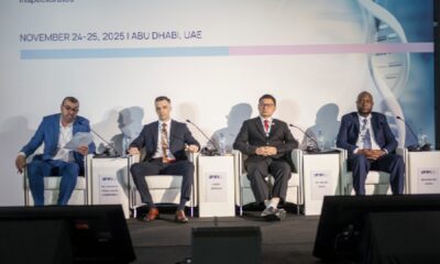 A man with short dark hair and a jacket is standing on a stage at a large conference, holding a microphone and addressing the audience with enthusiasm.