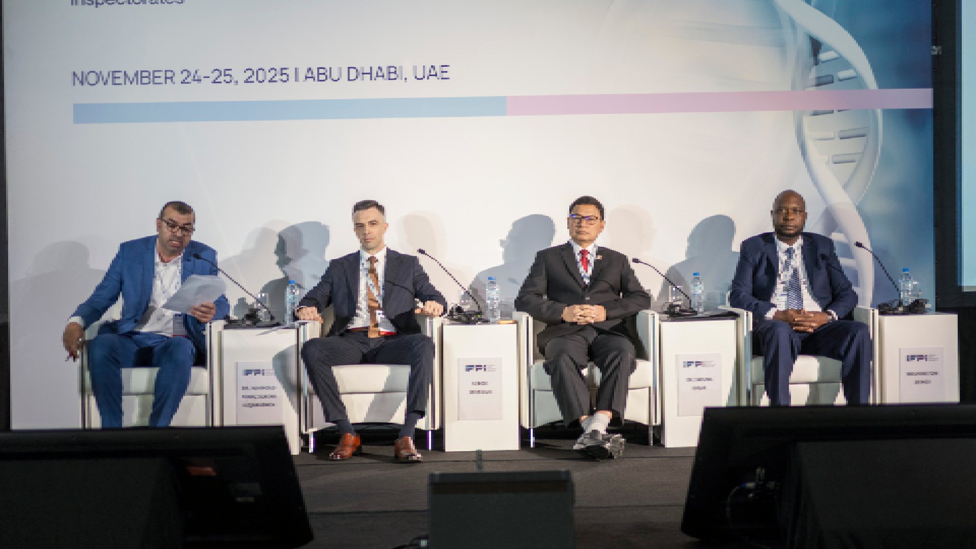 A man with short dark hair and a jacket is standing on a stage at a large conference, holding a microphone and addressing the audience with enthusiasm.