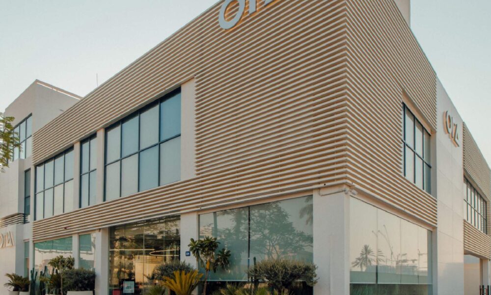A man in a dark suit is speaking passionately while holding a microphone on a stage in front of a large, diverse audience seated in a dark, formal auditorium.