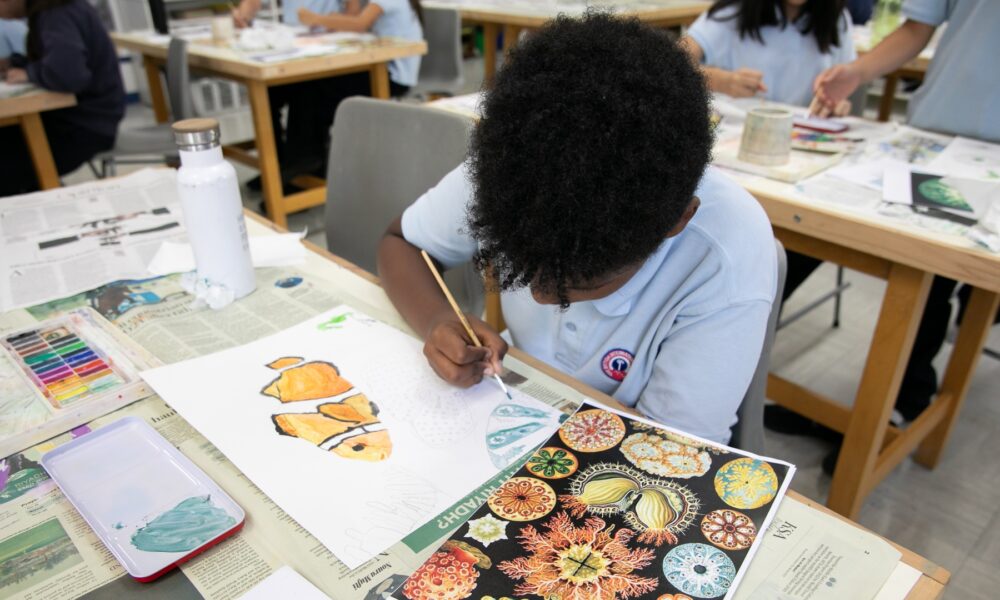 Top angle shot of a kid drawing in a classroom surrounded by other classmates.