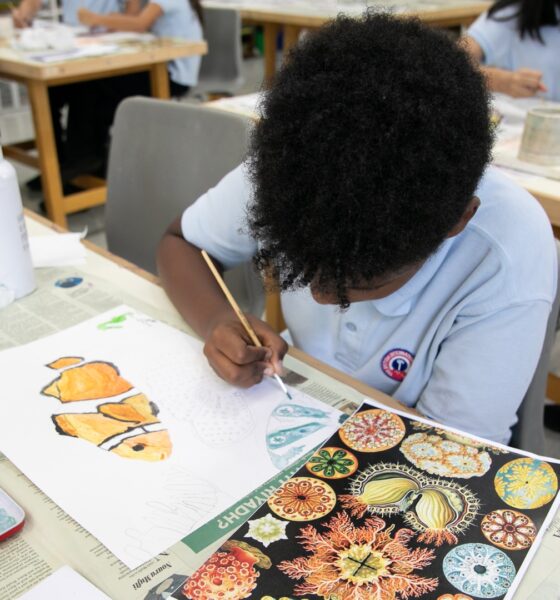 Top angle shot of a kid drawing in a classroom surrounded by other classmates.