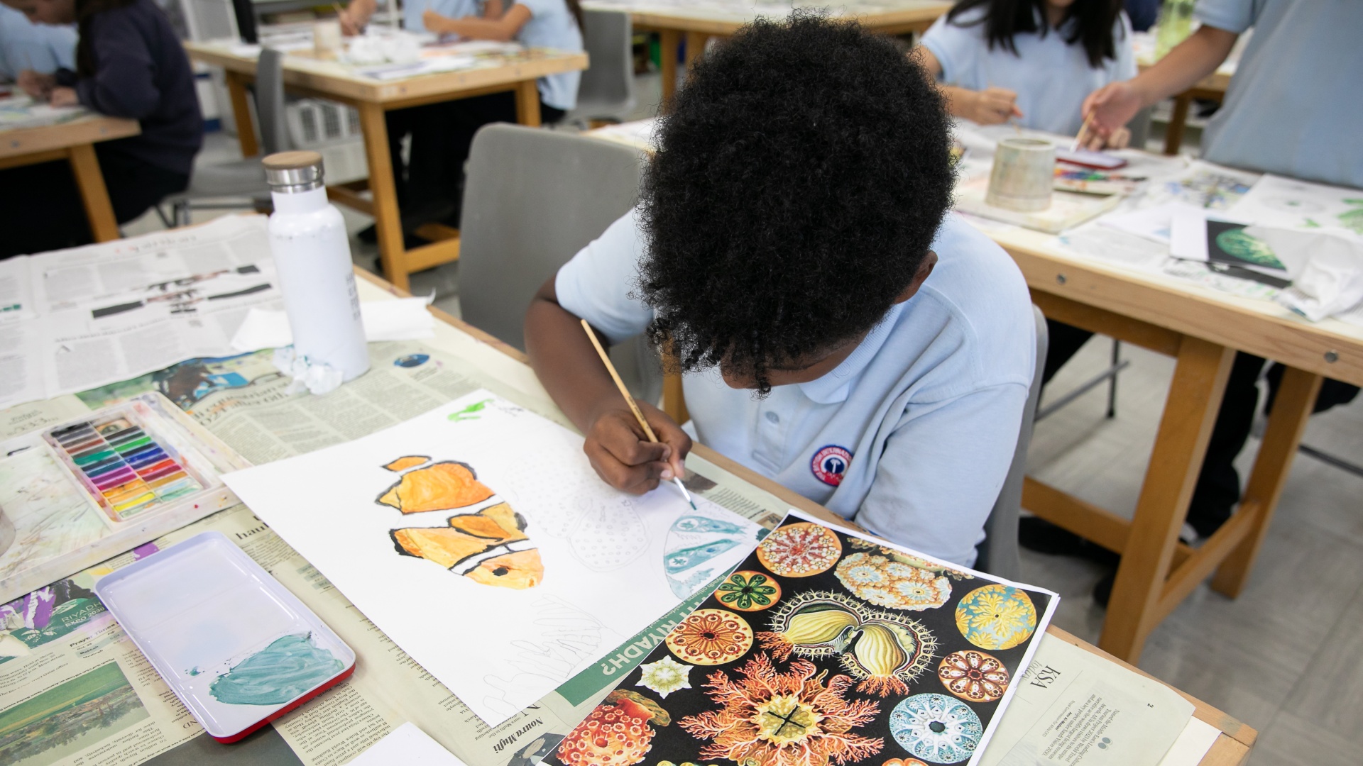 Top angle shot of a kid drawing in a classroom surrounded by other classmates.