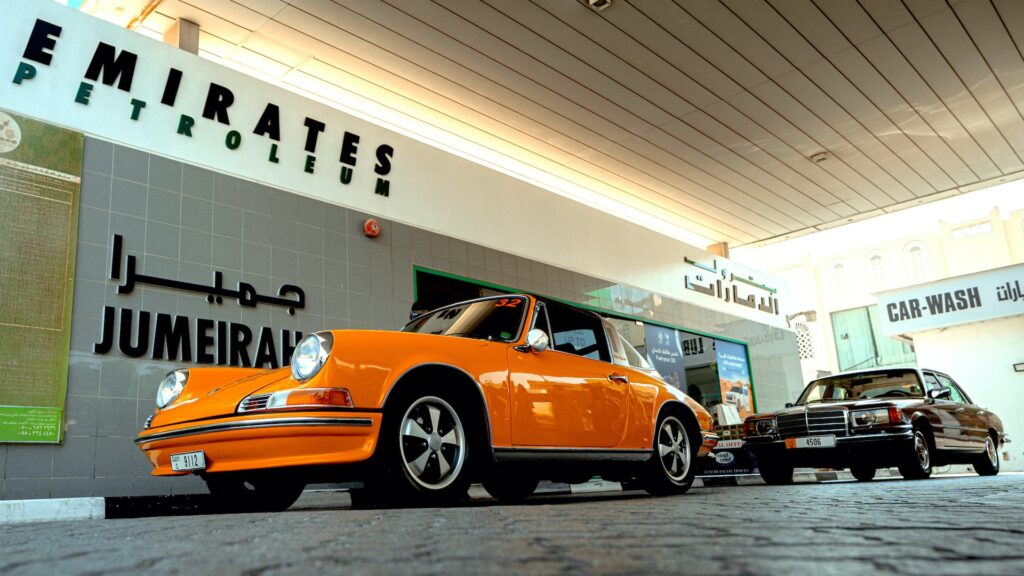 Low-angle view of an orange classic Porsche at an Emirates Petroleum Jumeirah gas station.