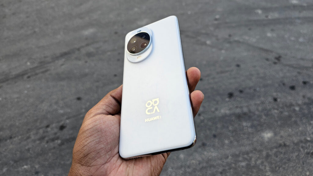 Angled view of the white Huawei Nova 14 Pro's back, held in a hand, showing the camera module and gold HUAWEI logo.