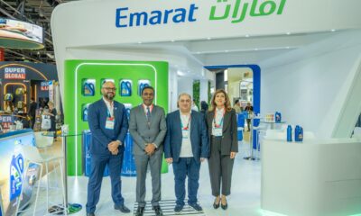 Four Emarat employees, two men and two women, pose in front of the branded Emarat exhibition booth displaying lubricant products.