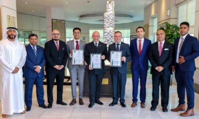 Group of executives standing indoors at Al Habtoor Grand Resort, holding framed ISO certification documents, with a modern decorative pillar in the background.