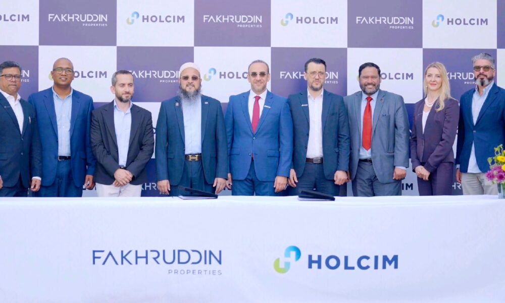 Fakhruddin Properties and Holcim UAE representatives standing behind a table with company logos during official MoU signing ceremony, with branded backdrop and floral arrangements on both sides.