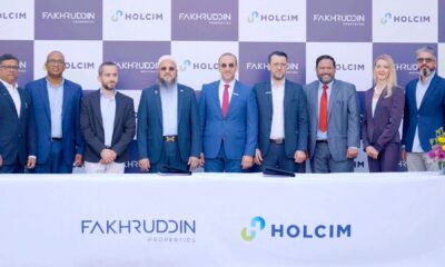 Fakhruddin Properties and Holcim UAE representatives standing behind a table with company logos during official MoU signing ceremony, with branded backdrop and floral arrangements on both sides.