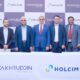 Fakhruddin Properties and Holcim UAE representatives standing behind a table with company logos during official MoU signing ceremony, with branded backdrop and floral arrangements on both sides.