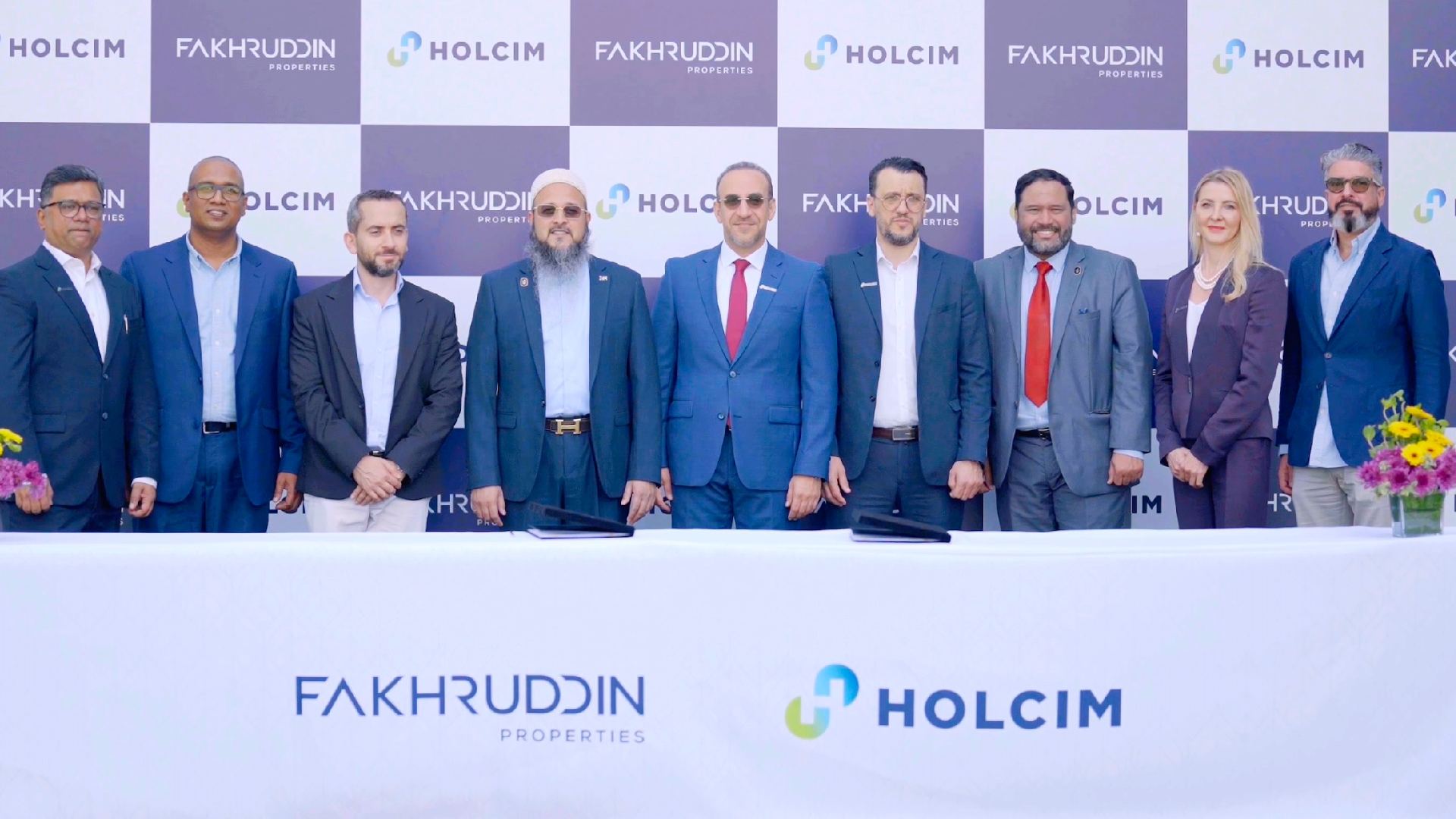 Fakhruddin Properties and Holcim UAE representatives standing behind a table with company logos during official MoU signing ceremony, with branded backdrop and floral arrangements on both sides.
