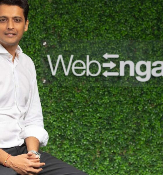 Person seated in front of a green artificial foliage wall featuring the WebEngage logo with a bird icon.