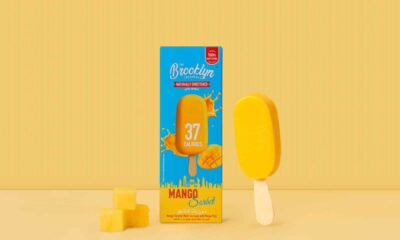 Mango sorbet bar from The Brooklyn Creamery displayed next to its bright blue and orange packaging that reads ‘37 Calories’ and ‘Mango Sorbet.’ The box features splashes of mango juice and a mango graphic, with three small mango cubes placed in front on a yellow background.