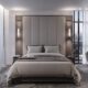 Modern luxury bedroom interior with a large upholstered headboard, neatly made bed with gray bedding, bedside tables with wall-mounted lights, floor-to-ceiling windows offering city skyline view, and a sleek dressing table with chair