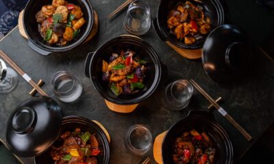 Five traditional Chinese claypot dishes served on a dark stone table at SHI restaurant, featuring vibrant vegetables, tender meats, and rich sauces in black claypots with wooden bases, surrounded by chopsticks, empty glasses, and lids