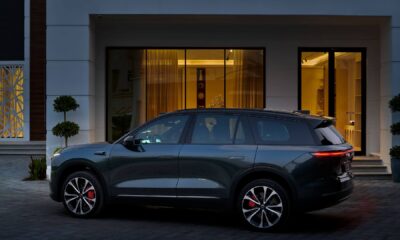 Side view of a dark gray NIO electric SUV parked on a paved driveway in front of a modern house with large glass doors and warm interior lighting.