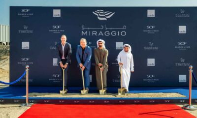 Source of Fate officials and partners participate in a ceremonial ground‑breaking for the Miraggio development on Al Marjan Island, holding shovels on a red carpeted site in front of a branded Miraggio and Source of Fate backdrop.