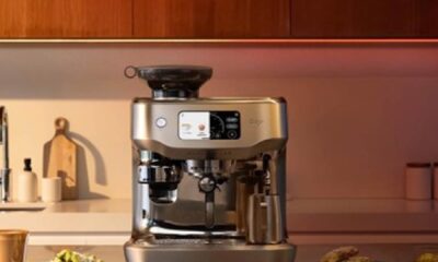 Sage Appliances Oracle Dual Boiler espresso machine on a modern kitchen countertop, featuring a touchscreen display and integrated grinder, with coffee cups and plated snacks placed nearby
