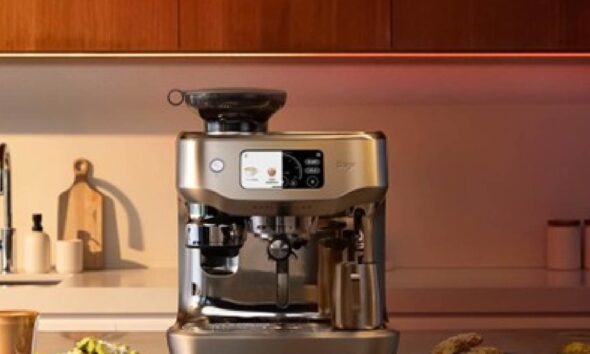 Sage Appliances Oracle Dual Boiler espresso machine on a modern kitchen countertop, featuring a touchscreen display and integrated grinder, with coffee cups and plated snacks placed nearby