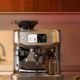 Sage Appliances Oracle Dual Boiler espresso machine on a modern kitchen countertop, featuring a touchscreen display and integrated grinder, with coffee cups and plated snacks placed nearby