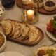 Overhead view of a BAB EL BAHR Suhoor table featuring freshly baked Arabic bread, scrambled eggs, hummus, foul medammas, labneh, pita bread, olives, herbs, and mixed Levantine dishes served with tableware and a lit candle.
