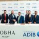 A group of executives from Sobha Realty and Abu Dhabi Islamic Bank stand together behind a signing table as representatives from both organizations shake hands in front of a branded backdrop displaying the Sobha Realty and ADIB logos, marking their partnership agreement.