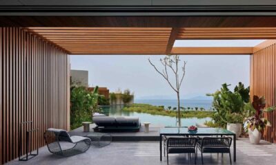 Covered outdoor terrace at Maxx Royal Bodrum Resort featuring a modern dining table and chairs, sun loungers facing a private infinity pool, wooden slatted pergola, lush landscaping, and panoramic sea view beyond the pool.