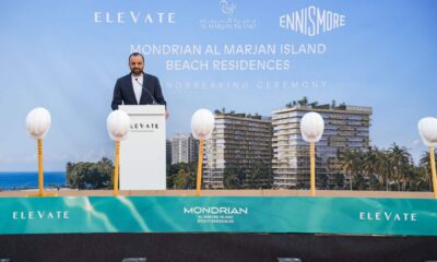 ELEVATE groundbreaking ceremony at Mondrian Al Marjan Island Beach Residences with a speaker at the podium, ceremonial shovels on stage, and a rendered beachfront residential development displayed on the backdrop
