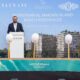 ELEVATE groundbreaking ceremony at Mondrian Al Marjan Island Beach Residences with a speaker at the podium, ceremonial shovels on stage, and a rendered beachfront residential development displayed on the backdrop