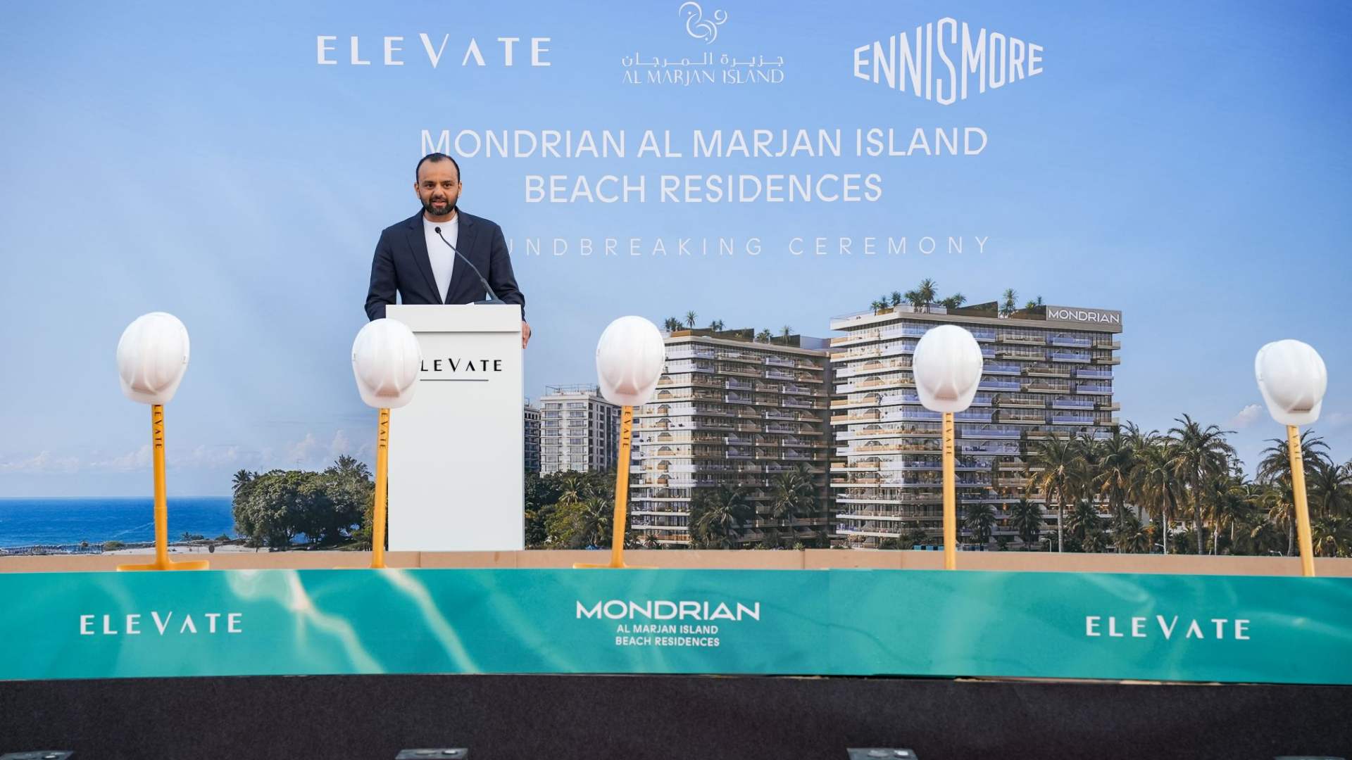 ELEVATE groundbreaking ceremony at Mondrian Al Marjan Island Beach Residences with a speaker at the podium, ceremonial shovels on stage, and a rendered beachfront residential development displayed on the backdrop