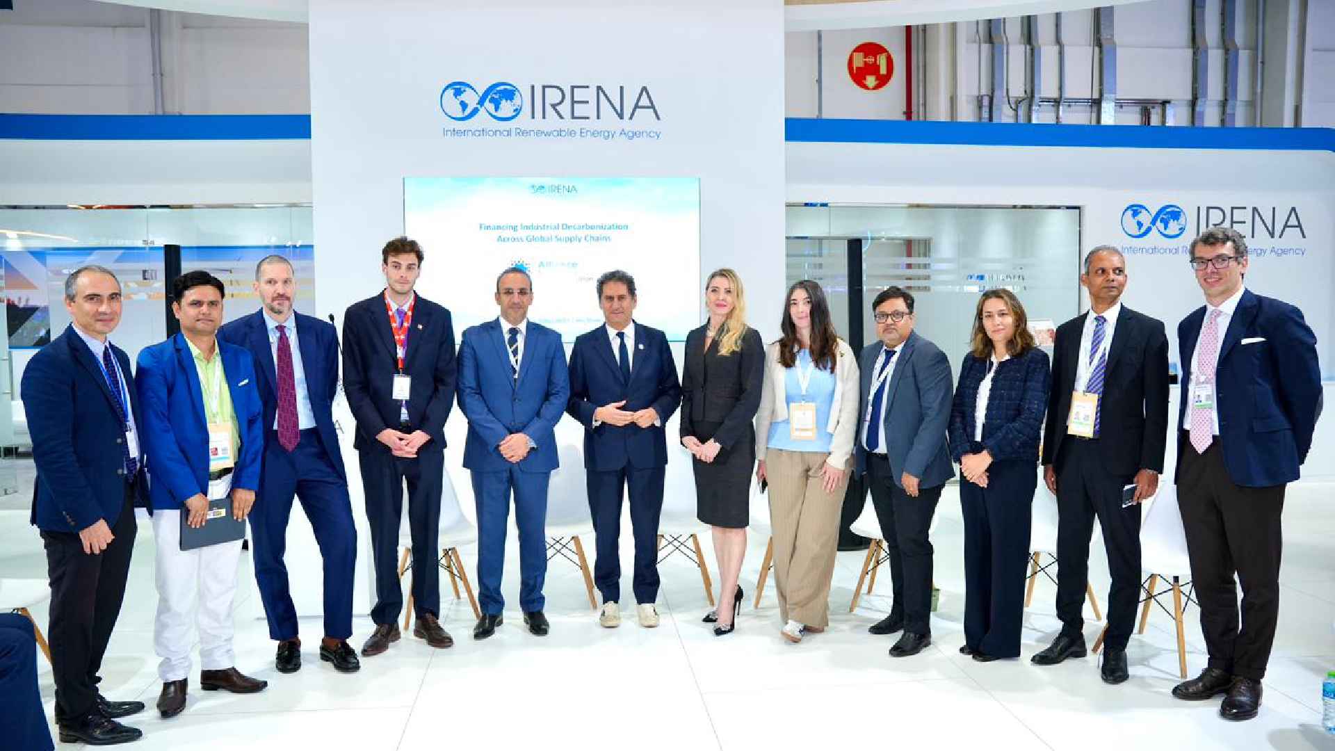 HOLCIM UAE delegation standing with industry stakeholders at the IRENA pavilion during an official alliance announcement event, with IRENA branding displayed in the background.