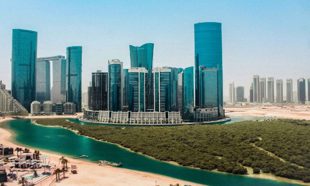 Aerial view of Al Reem Island showing modern high-rise towers along a waterfront canal, sandy shoreline, and landscaped mangrove area in Abu Dhabi by OBJECT 1.