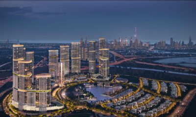Aerial night view of Sobha Realty master-planned waterfront community featuring illuminated high-rise towers, residential villas, landscaped roads, and Dubai skyline in the background